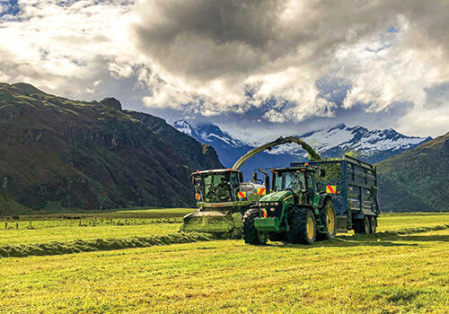 A harvester collecting silage surrounded by snow topped mountains