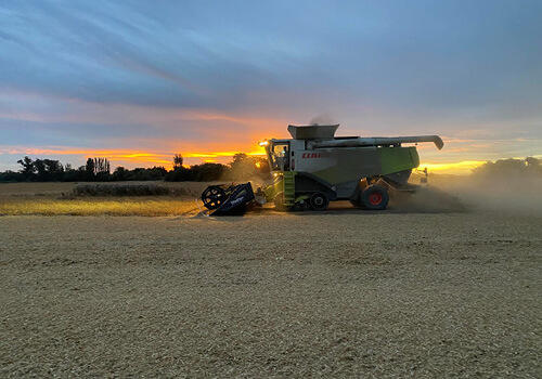 a harvester finishes it's last row of wheat harvesting while the sun sets in the background
