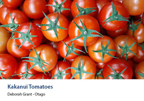 A close-up view of bright red Kakanui tomatoes piled closely together, showing their glossy skins and green tops. Caption: Deborah Grant, Otago.