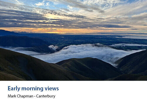 A vast mountainous landscape with a cloud-filled valley under a moody blue and orange morning sky. Caption: Mark Chapman, Canterbury.