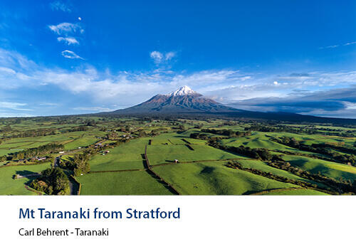 Aerial view of lush green farmland stretching toward the iconic snow-capped cone of Mt Taranaki. Caption: Carl Behrent, Taranaki.