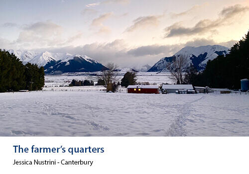 A snowy homestead scene with red farm buildings set against snow-covered paddocks and rugged mountains. Caption: Jessica Nustrini, Canterbury.