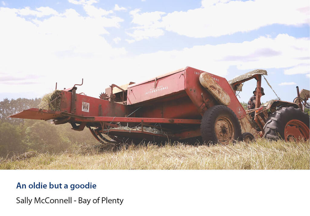 Vintage square baler working behind a tractor in a hay paddock.