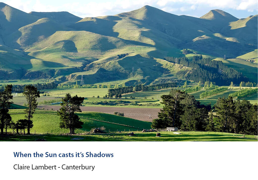 Sun and shadow across steep hills above rolling green farmland and trees.