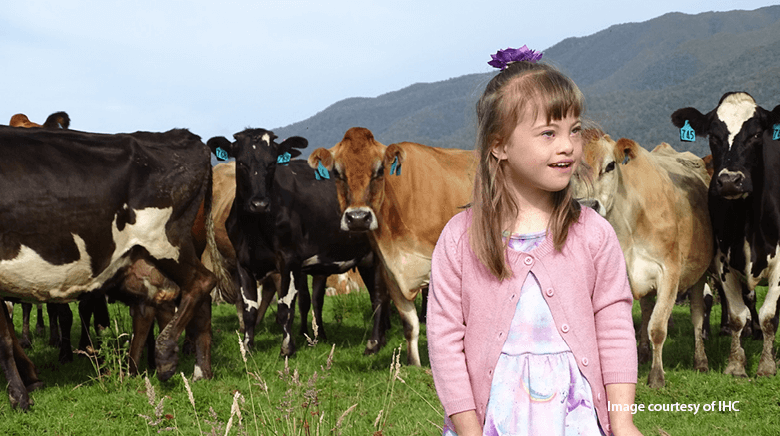 Smiling young girl with Down's Syndrome standing in a field with cows in the background